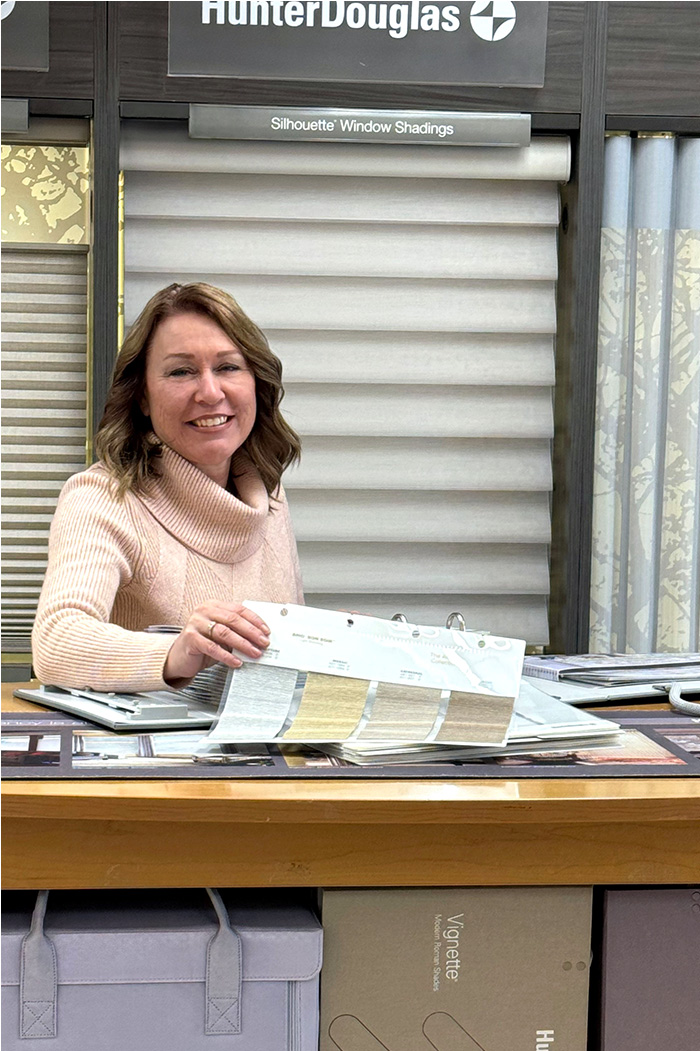 Jean, works for Excelsior Paint and Design in Excelsior, Minnesota. Jean is standing in front of the Hunter Douglas window shadings display.